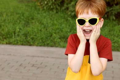 Cute little boy with sunglasses in park, space for text