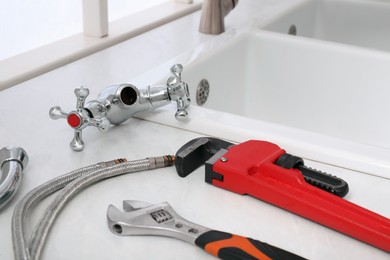 Photo of Parts of water tap and wrenches on white marble countertop in kitchen