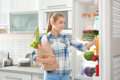 Photo of Woman putting products into refrigerator in kitchen