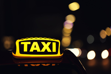 Photo of Taxi car with yellow roof sign on city street at night, closeup