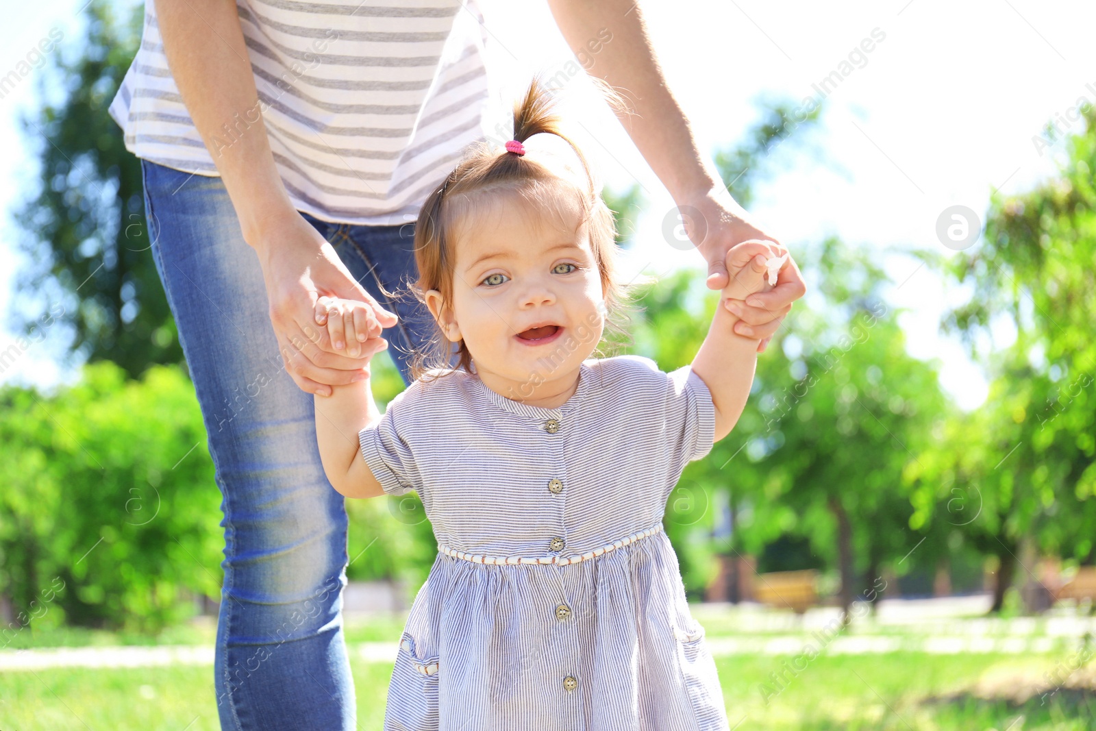 Photo of Adorable baby girl holding mother's hands while learning to walk outdoors