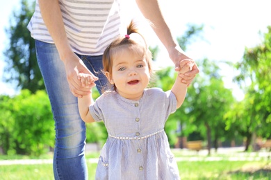 Adorable baby girl holding mother's hands while learning to walk outdoors