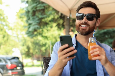Photo of Handsome man with bottle of delicious juice in outdoor cafe. Space for text