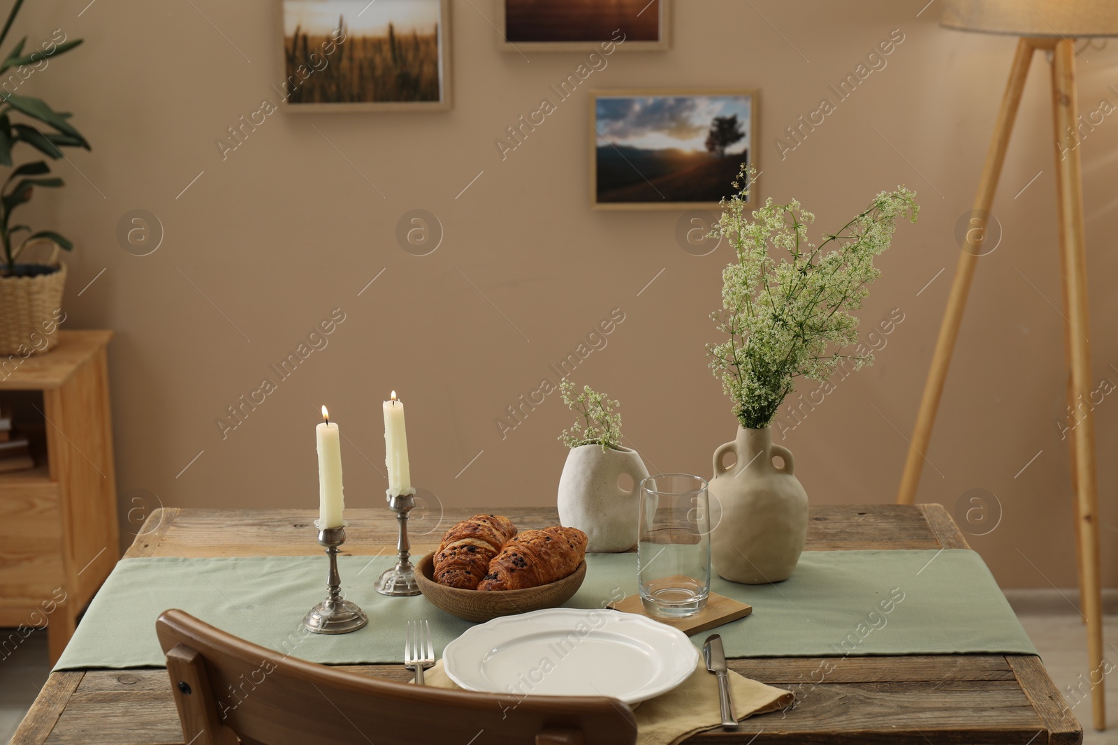 Photo of Clean tableware, candlesticks, flowers and fresh pastries on table in stylish dining room