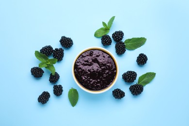 Photo of Blackberry puree in bowl and fresh berries with mint on light blue background, flat lay