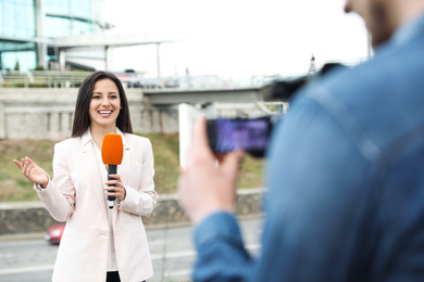 Young journalist and video operator working on city street