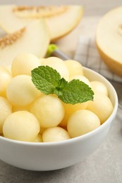 Photo of Melon balls and mint in bowl on light grey table, closeup