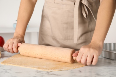 Photo of Woman rolling dough for traditional English apple pie at white marble table, closeup