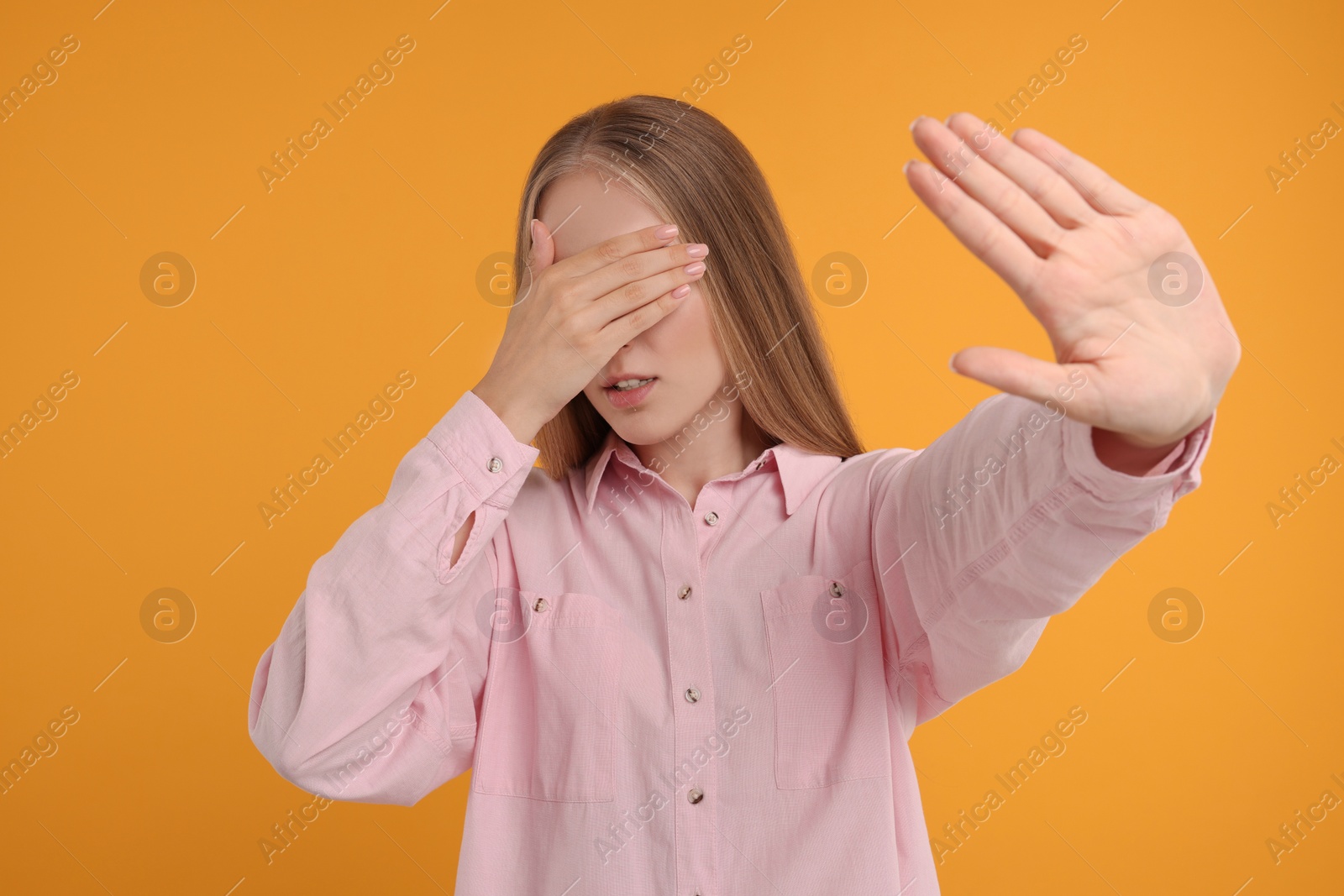 Photo of Embarrassed woman covering face with hand on orange background
