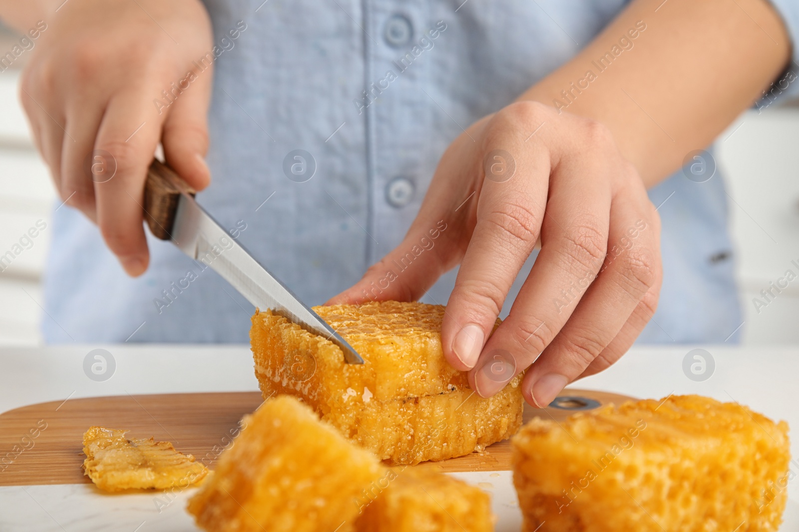 Photo of Woman cutting fresh honeycomb at table, closeup