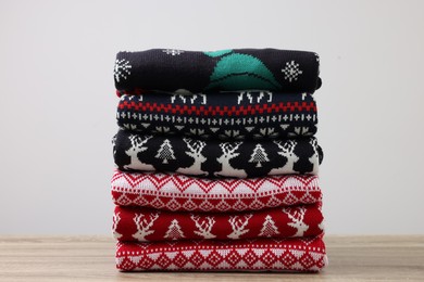 Photo of Stack of different Christmas sweaters on wooden table against light background