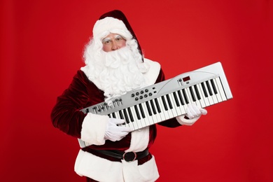 Photo of Santa Claus with synthesizer on red background. Christmas music