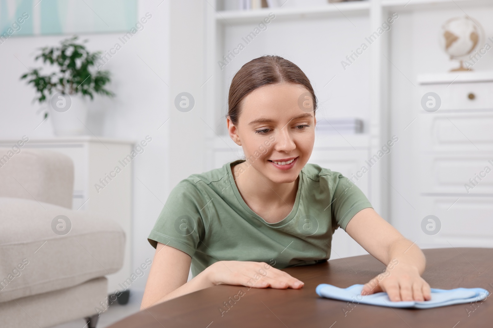 Photo of Woman with microfiber cloth cleaning wooden table in room