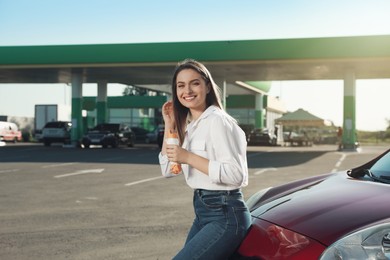 Photo of Beautiful young woman with hot dog near car at gas station