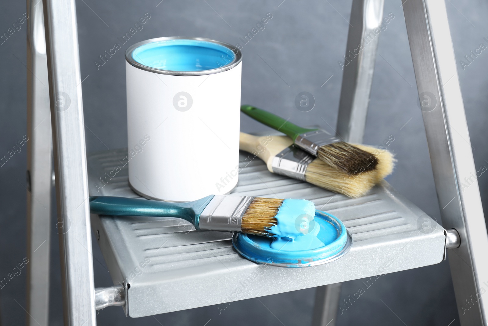 Photo of Can of light blue paint and brushes on metal ladder