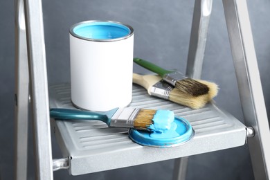 Can of light blue paint and brushes on metal ladder