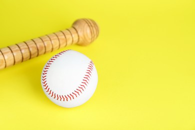 Photo of Wooden baseball bat and ball on yellow background, space for text. Sports equipment