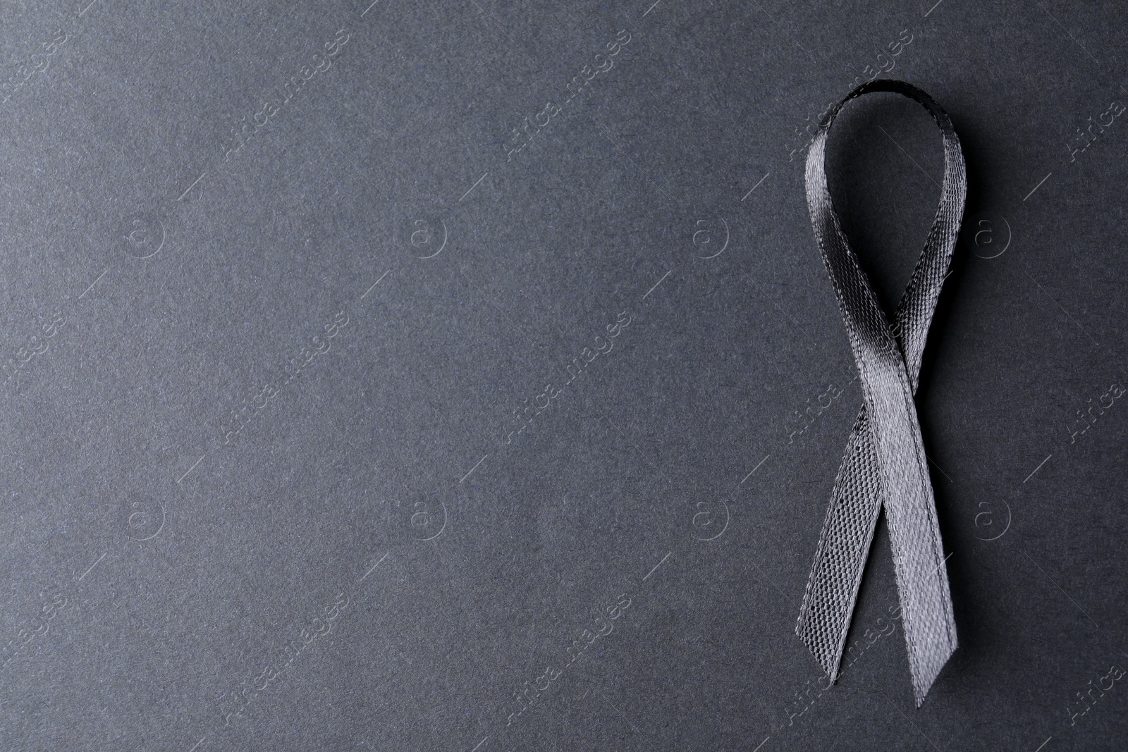 Photo of Black ribbon on dark background, top view with space for text. Funeral symbol