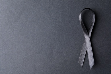 Black ribbon on dark background, top view with space for text. Funeral symbol