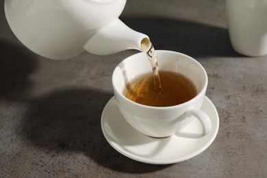 Photo of Pouring aromatic tea in cup at gray table, closeup