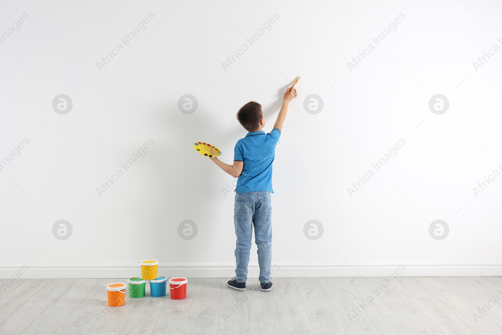 Photo of Little child painting on white wall indoors