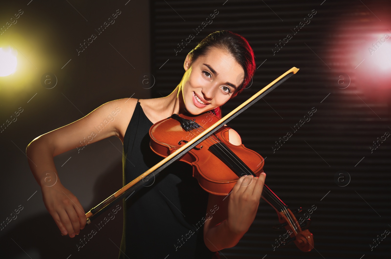 Photo of Beautiful young woman playing violin in dark room