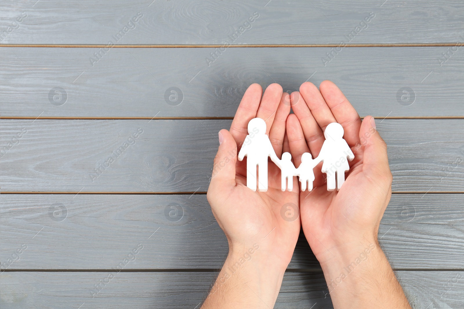 Photo of Young man holding family figure in his hands against grey wooden background, top view. Space for text