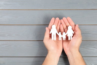 Photo of Young man holding family figure in his hands against grey wooden background, top view. Space for text