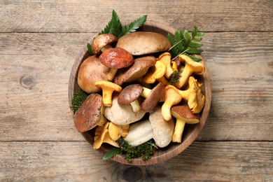 Photo of Bowl with different mushrooms on wooden table, top view