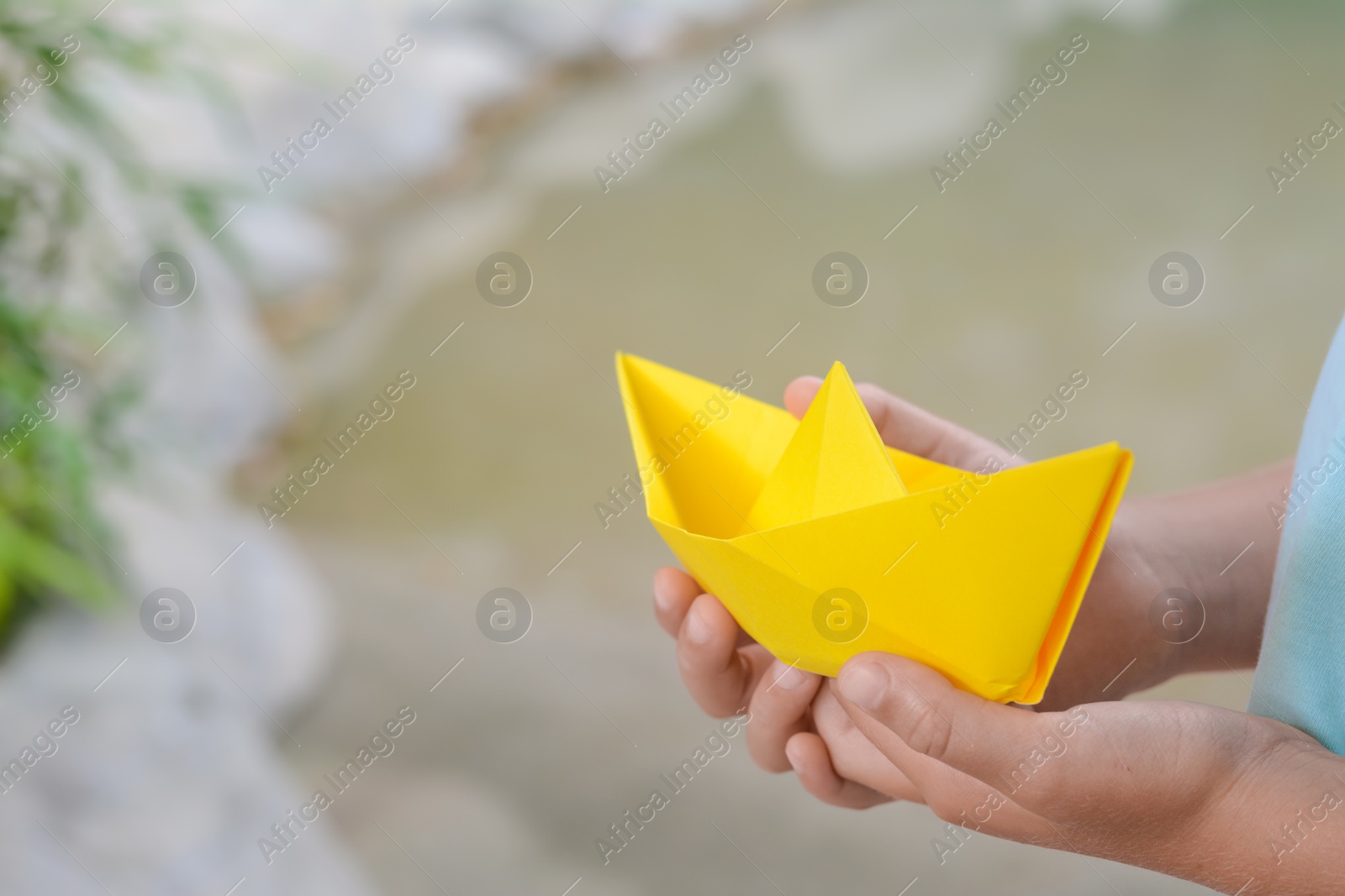 Photo of Little girl holding yellow paper boat outdoors, closeup. Space for text