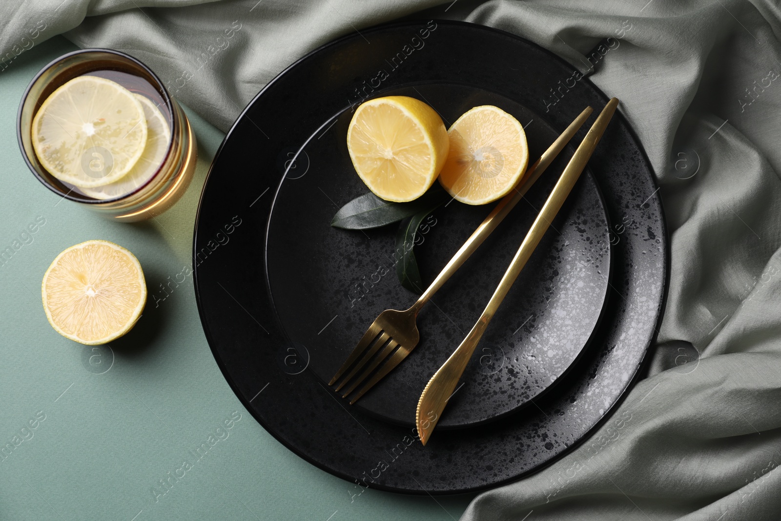 Photo of Stylish table setting. Plates, cutlery and tea with lemon on olive background, top view