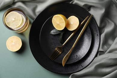 Stylish table setting. Plates, cutlery and tea with lemon on olive background, top view