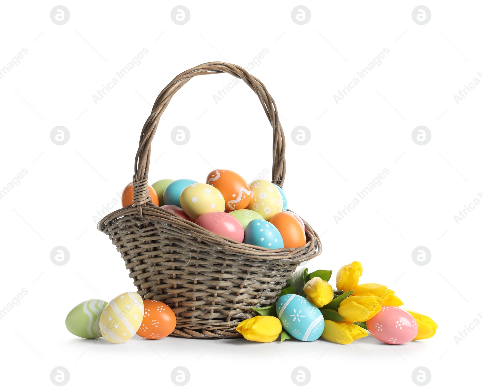 Photo of Wicker basket with painted Easter eggs and spring flowers on white background