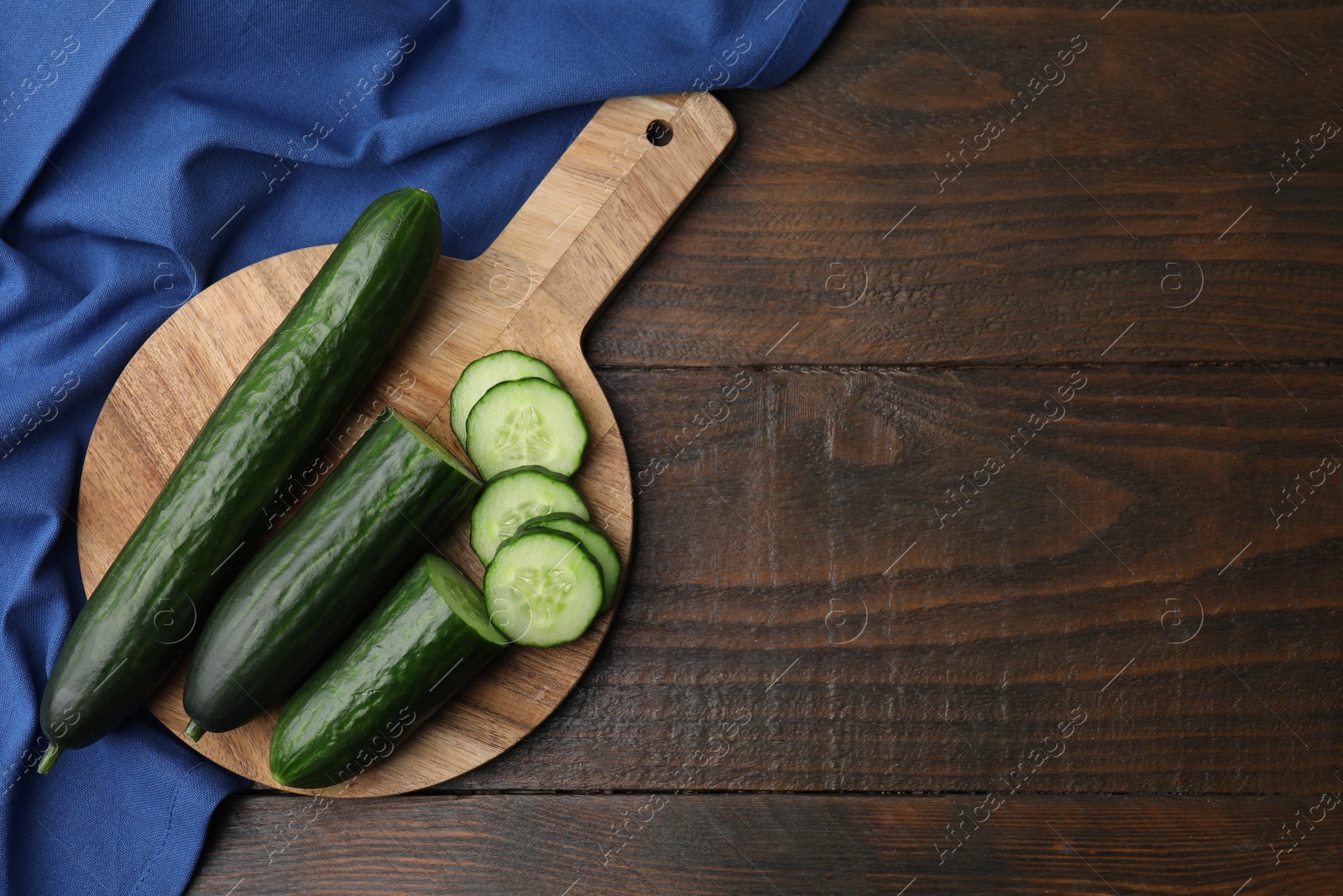 Photo of Fresh whole and cut cucumbers on wooden table, top view. Space for text