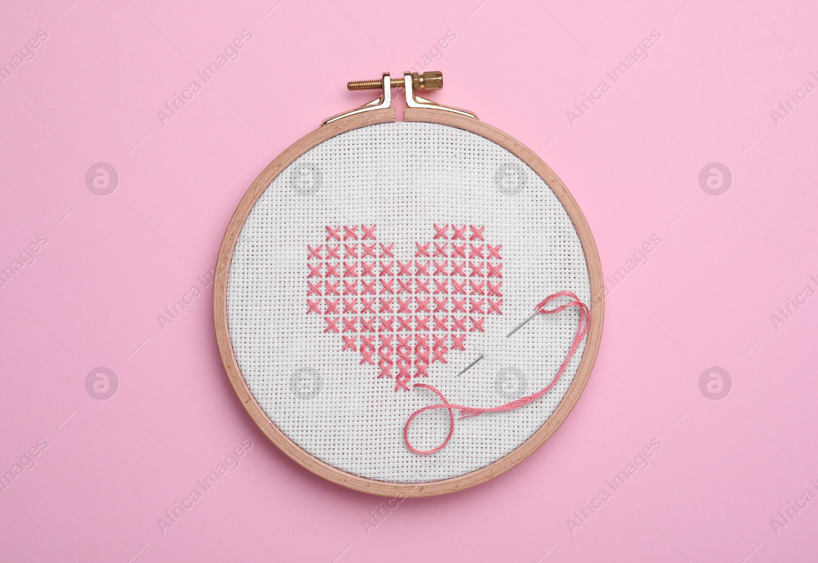 Photo of Canvas with embroidered heart and needle in hoop on pink background, top view