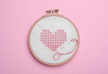 Photo of Canvas with embroidered heart and needle in hoop on pink background, top view