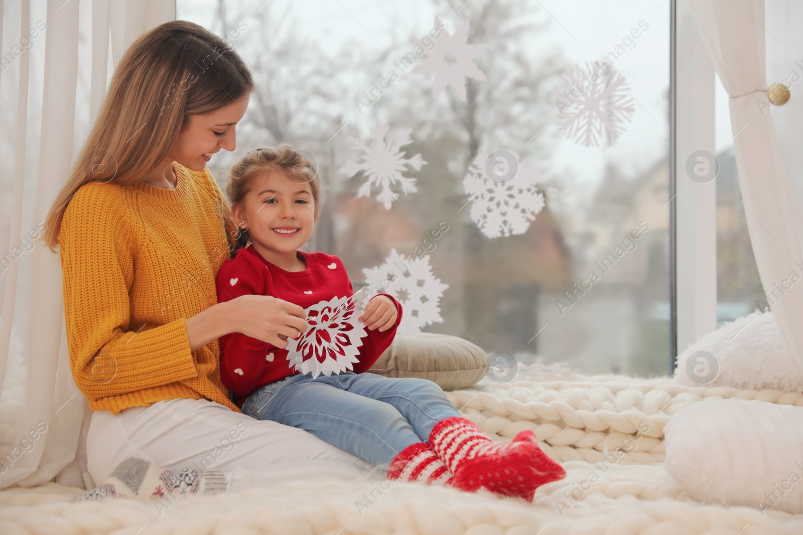 Photo of Happy mother and daughter with paper snowflake near window indoors