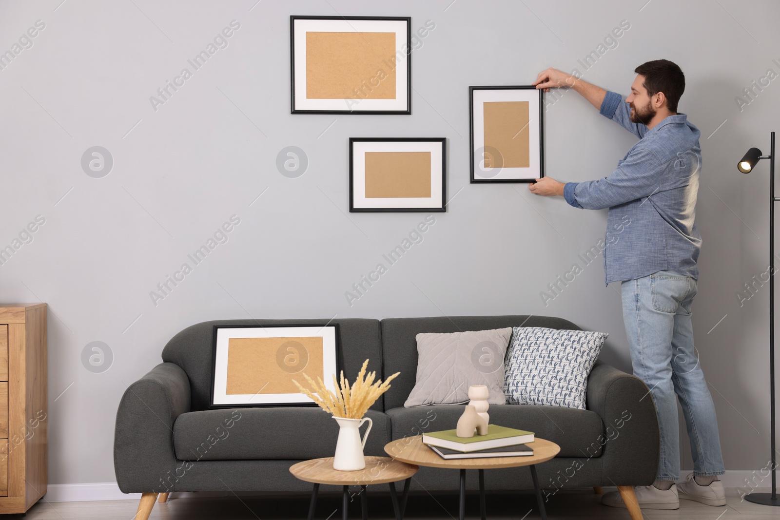 Photo of Man hanging picture frame on gray wall at home