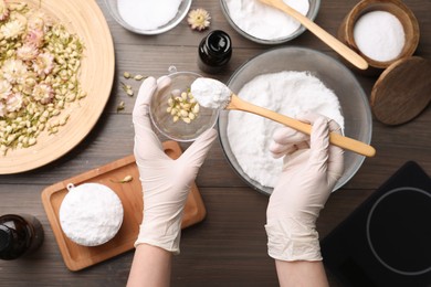 Woman in gloves making bath bomb at wooden table, top view