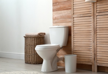 Toilet bowl near wooden wall in modern bathroom interior