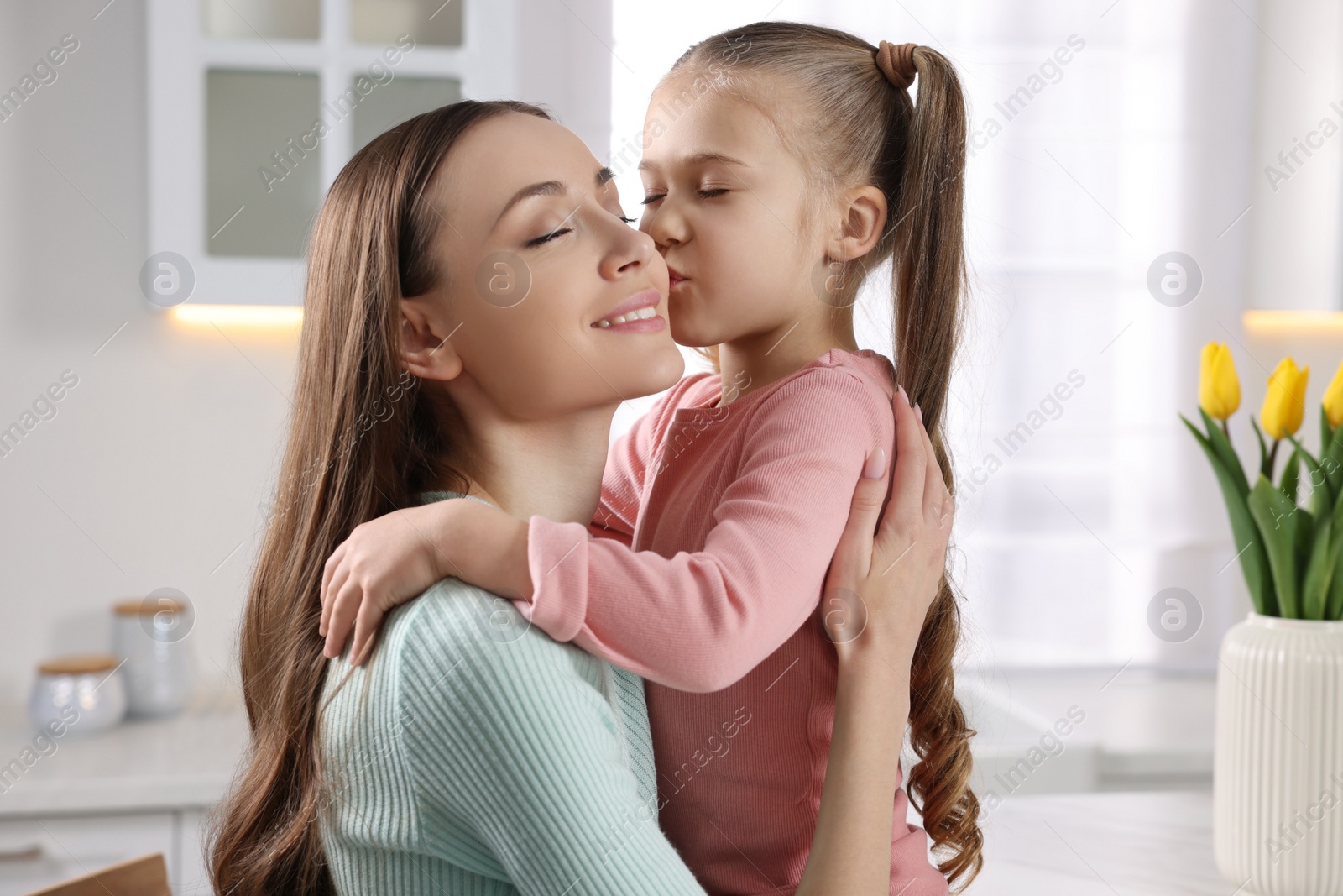 Photo of Cute daughter kissing her mom in kitchen