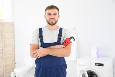 Photo of Young plumber with wrench near washing machine in bathroom