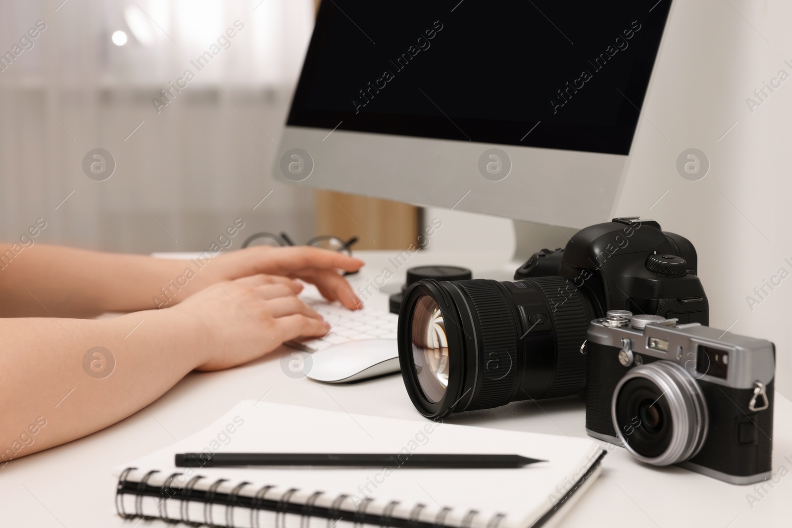 Photo of Photographer working on computer at white table with cameras indoors, closeup