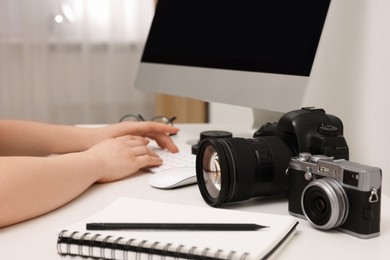 Photographer working on computer at white table with cameras indoors, closeup