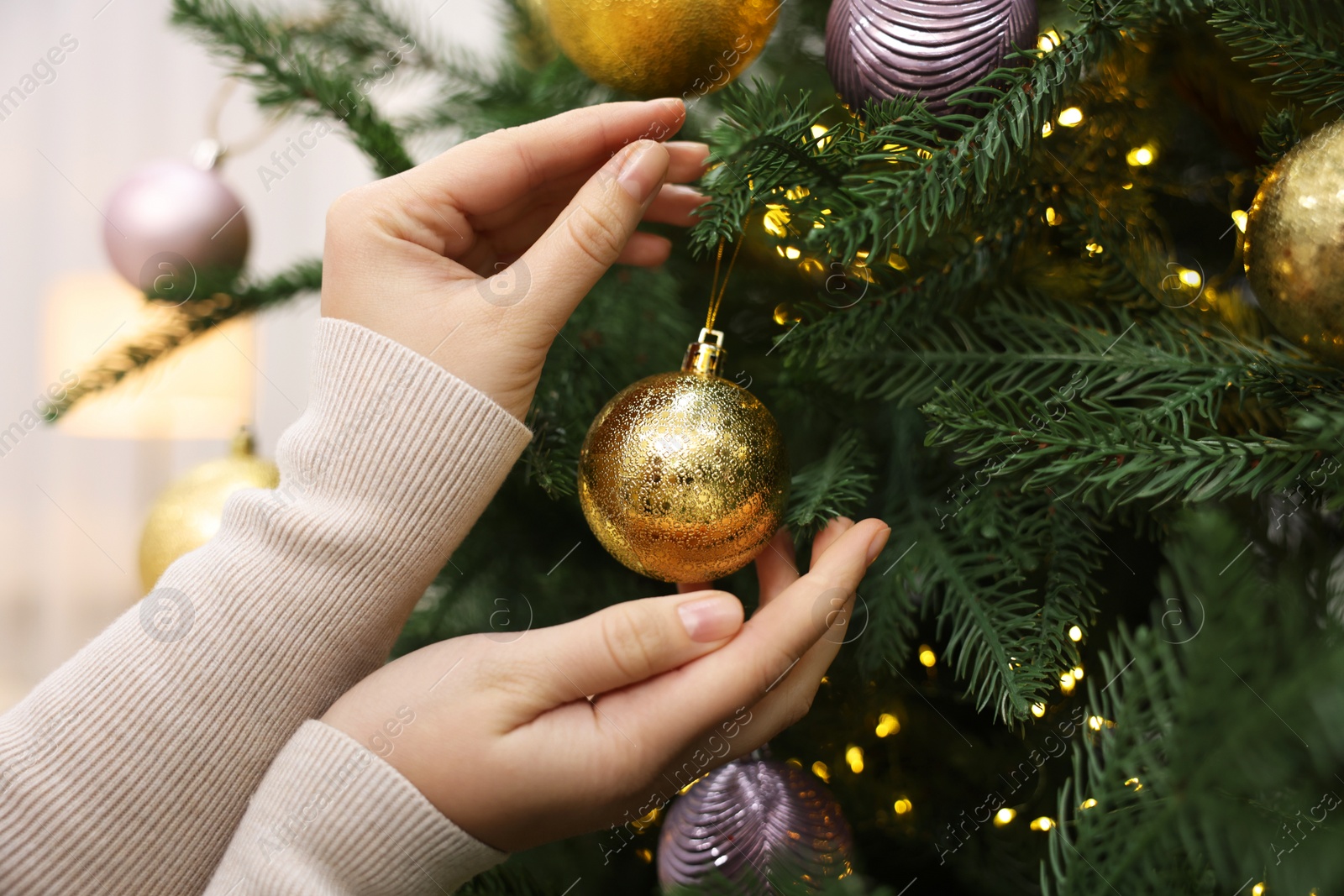 Photo of Woman decorating fir tree with golden Christmas ball indoors, closeup