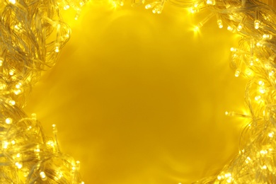 Frame made of glowing Christmas lights on yellow background, top view. Space for text