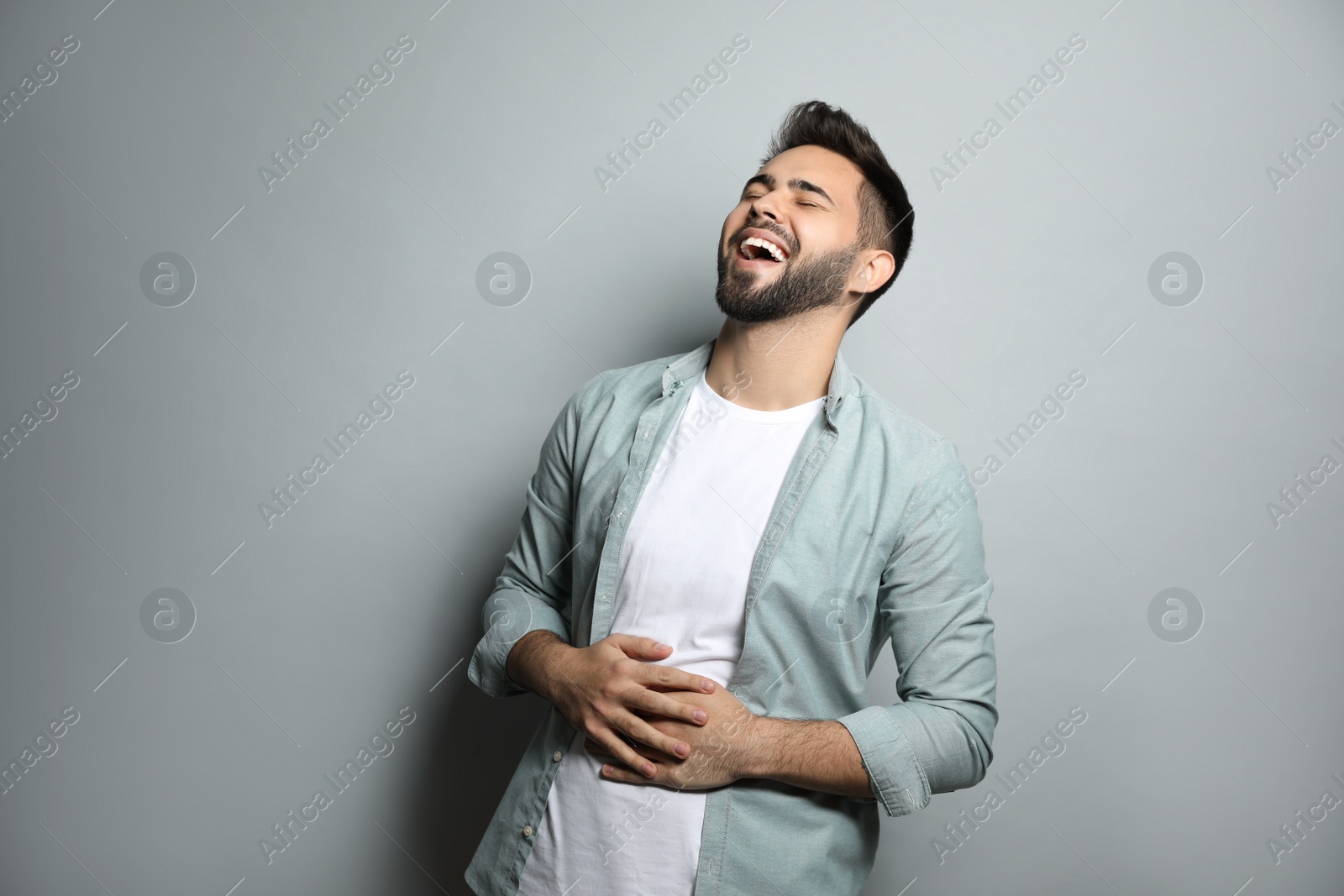 Photo of Young man laughing on light grey background. Funny joke