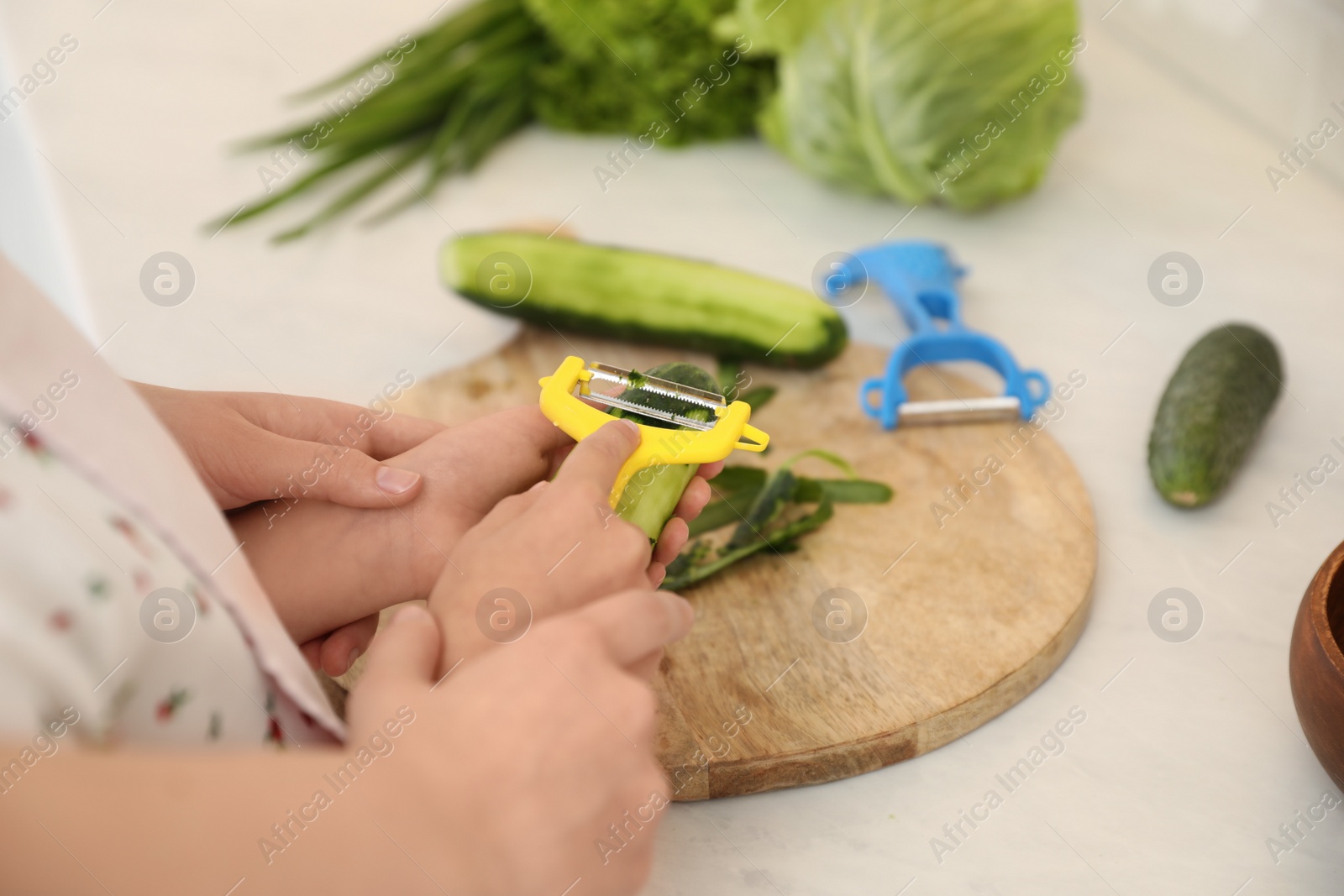 Photo of Mother teaching daughter to peel vegetable at kitchen counter, closeup