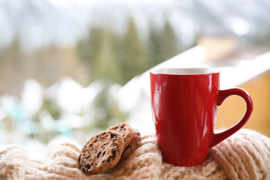 Photo of Fresh coffee, tasty cookies and knitted fabric outdoors on winter morning. Space for text