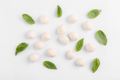 Photo of Tasty mozzarella balls and basil leaves on white background, flat lay